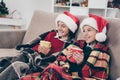 Photo of two cheerful relaxed children sit comfy couch enjoy x-mas eve cacao wear jumper hat in decorated home indoors