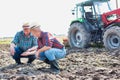 Photo of Two farmers examining soil at farm against tractor