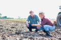 Photo of Two farmers examining soil at farm against tractor