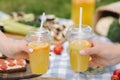 Photo of two hand hold orange lemonade in front of vegan picnic outdoors. Healthy food concept Royalty Free Stock Photo