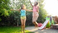 Photo of two happy laughing sisters in wet clothes dancing under water droplets from garden hose at garden. Family Royalty Free Stock Photo