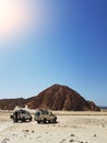 Photo of two jeeps on background of mountain, sand blue sky