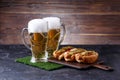 Photo of two mugs of foam beer, green grass with football, hotdogs