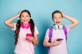 Photo of two nice positive surprised friends wearing headphones using telephones isolated over blue color background