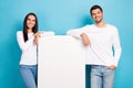 Photo of two optimistic satisfied pleasant couple people wear white shirts lean on big white billboard isolated on blue Royalty Free Stock Photo