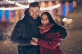 Photo of two people visiting central city park at x-mas eve standing close wearing warm winter jackets and scarfs feel