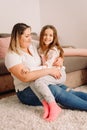 Photo of two persons mother and daughter passing time together at home sitting on the carpet, mother holding her little