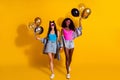 Photo of two pretty charming young girlfriends wear denim clothes dark glasses holding balloons isolated yellow color Royalty Free Stock Photo