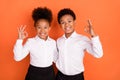 Photo of two young afro kids happy positive smile show okay alright sign cool advert isolated over orange color Royalty Free Stock Photo