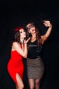 Photo of two young party women smiling taking selfie photo on mobile phone over black background Royalty Free Stock Photo