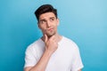 Photo of unsure suspicious guy wear white t-shirt hand arm chin looking empty space isolated blue color background