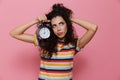 Photo of upset woman 20s with curly hair holding alarm clock, is