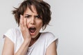 Photo of upset woman with short brown hair in basic t-shirt keeping hand over her face and screaming at camera Royalty Free Stock Photo