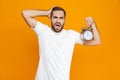 Photo of uptight man 30s in casual wear holding alarm clock, isolated over yellow background