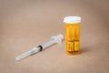 Vials of Naloxone in an orange plastic prescription bottle and syringe in front of seamless plain background