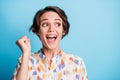 Photo of victorious amazed delighted young woman raise fist look empty space isolated on blue color background