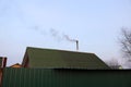 The texture of a green iron roof with a Smoking chimney above a green metal fence against the evening sky. Royalty Free Stock Photo