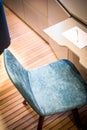 A blue chair at a desk table on a yacht as a working corner with paper and pen, with wooden floor in the background