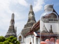 A water bottle with a Wat Arun sticker held up against the real temple in Bangkok, Thailand