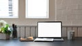 Photo of white blank screen laptop putting on the modern working desk including potted plant, coffee cup, notebook, pencil holder. Royalty Free Stock Photo