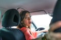 Photo of a woman in car indoor keeps wheel, turning around looking at passengers in back seat idea taxi driver. Concept of exam Royalty Free Stock Photo