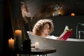 Photo of a woman reading a book with a red cover while lying in the bath. A woman spends a pleasant evening taking a Royalty Free Stock Photo