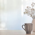 A photo of a wooden desk with a white vase with dried white flowers and a gray cup