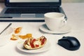 A photo of workplace after breakfast. A cup of coffee with laptop on white tablecloth, empty bowl with porridge leftovers, half of