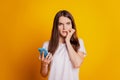 Photo of worried lady bite nails hold phone wear white t-shirt posing on yellow background Royalty Free Stock Photo