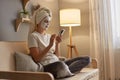 Photo of young adorable woman in white towel sitting on sofa with crossed legs at home doing face cleaning procedures and using