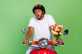 Photo of young afro man afraid scared worried hold bunch of tulips ride motor bike isolated over green color background