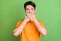 Photo of young amazed afraid man cover hands mouth tell secret mistake isolated on green color background