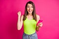 Photo of young amazed lady hold cell phone open mouth raise fist wear green top isolated vibrant pink color background Royalty Free Stock Photo
