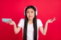 Photo of young asian girl unhappy moody uncertain dislike music earphones use cellphone isolated over red color Royalty Free Stock Photo