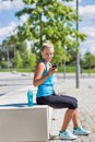 Portrait of young attractive woman sitting while using and listening to music on her smartphone in park Royalty Free Stock Photo