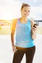 Portrait of young attractive woman standing while using and listening to music on her smartphone in park Royalty Free Stock Photo