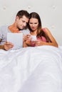 Portrait of young attractive woman showing smartphone while his boyfriend playing games on his digital tablet in bed