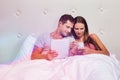 Portrait of young attractive woman showing smartphone while his boyfriend playing games on his digital tablet in bed