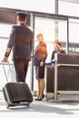 Portrait of young beautiful airport staff opening the gate for boarding while mature pilot walking in airport