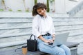 Beautiful cute woman sitting outdoors using laptop computer talking by phone Royalty Free Stock Photo