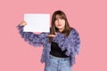 Photo of a young beautiful dark-haired woman with bangs looks into frame, holds blank sheet of paper for inscriptions. Shows Royalty Free Stock Photo