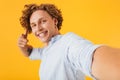 Photo of young beautiful man 20s taking selfie photo and pointing finger at camera, isolated over yellow background Royalty Free Stock Photo