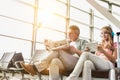 Young beautiful teenage girl watching movie on digital tablet with headphones on while her father is reading newspaper in airport Royalty Free Stock Photo