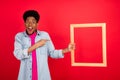 Photo of young black guy point finger wooden frame advert select promo recommend isolated over red color background Royalty Free Stock Photo