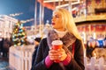 Photo of young blonde with glass in hands on background of carousel in evening for walk Royalty Free Stock Photo