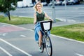 Photo of young blonde in long denim skirt riding bike on road in city Royalty Free Stock Photo