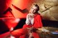 Photo of young blonde in red jacket looking up sitting on sofa at table Royalty Free Stock Photo