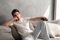 Photo of young bored man sitting on couch at home, and changing