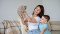 Photo of a young brunette and a 7-years boy playing with a gray kitten sitting on a sofa in a flat Royalty Free Stock Photo