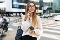 Photo of young caucasian woman talking on cellphone and holding paper cup while walking in big city street Royalty Free Stock Photo